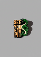 Enamel pin of “See You in the Pit” text next to snake on grey background 