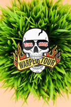 Skull with sunglass that read "Vans 2025" biting a sign that reads "Warped Tour" on grass background